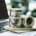 image of rolled cash on laptop to illustrate how to invest $10k