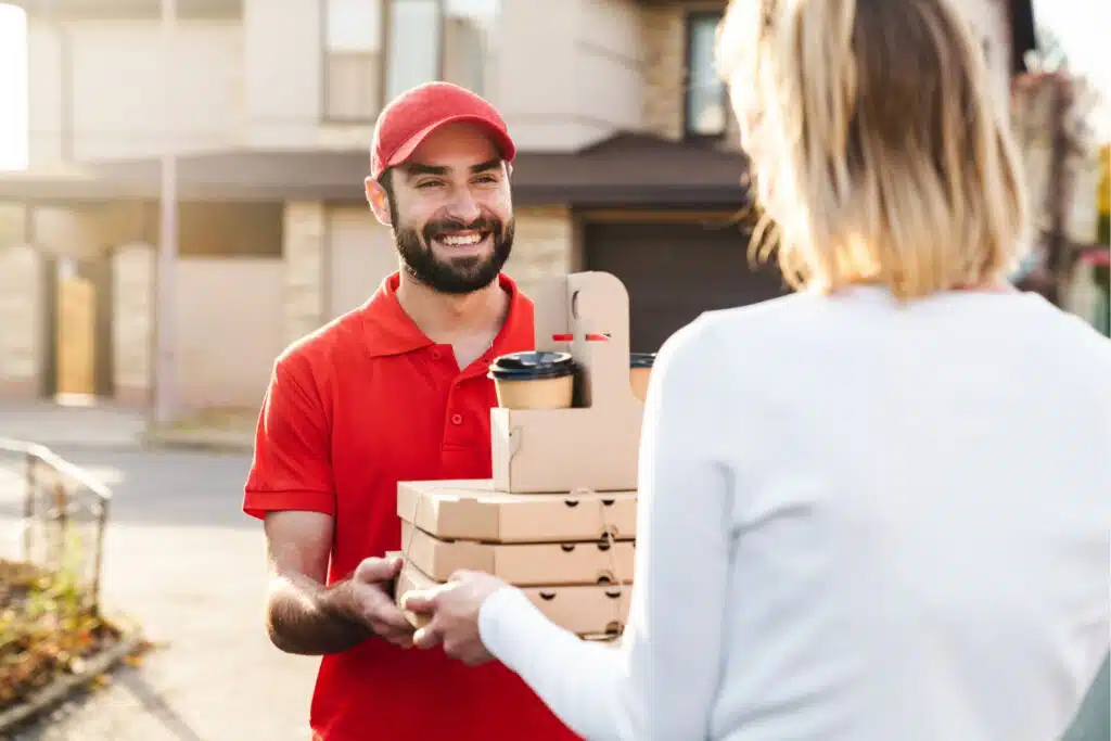 a food delivery driver handing boxes of food to a woman in her driveway