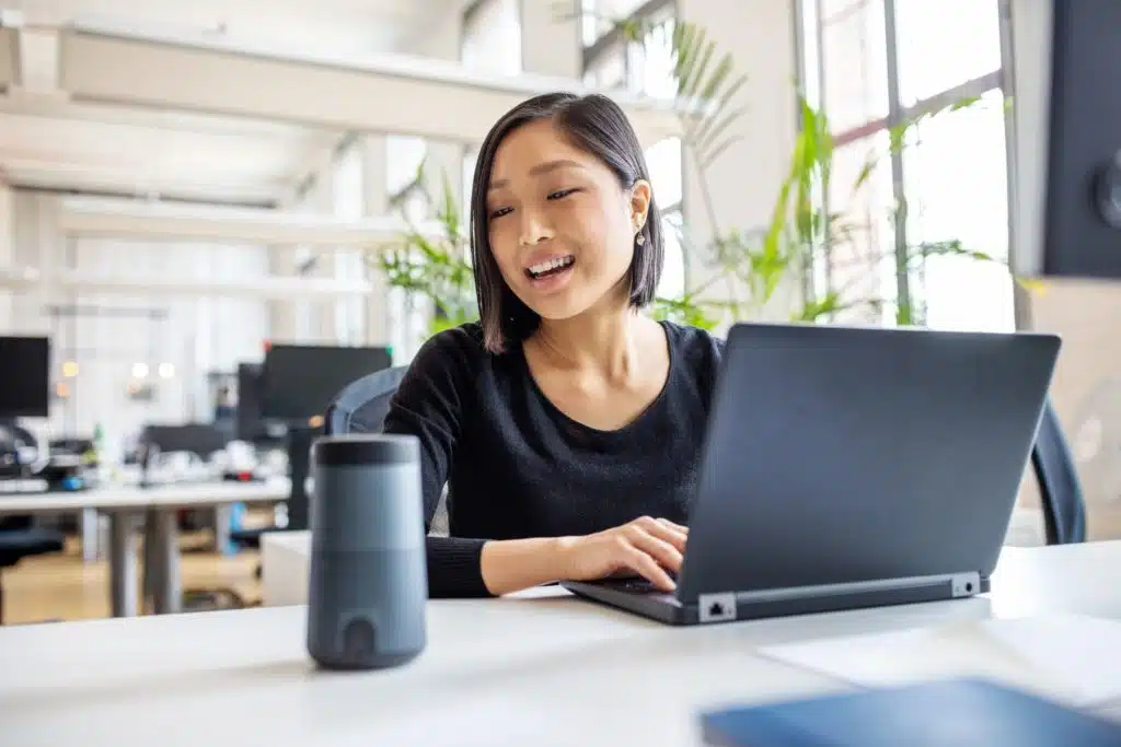 Woman sitting at a desk with a laptop speaking into an Alexa device